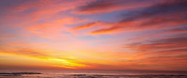 Dramatic Atlantic Ocean sunrise with vivid orange, red, and purple clouds stretching across a wide beach