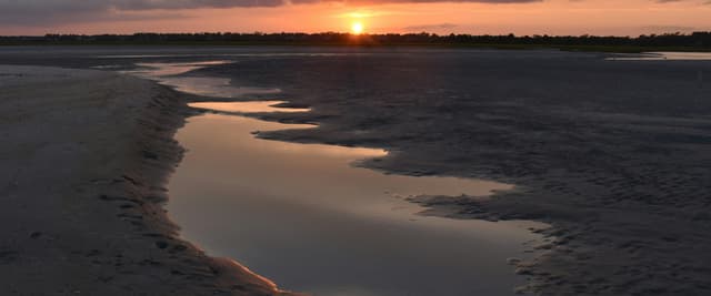 NC coastal tidal flat at sunset with winding water reflection and dramatic orange sky