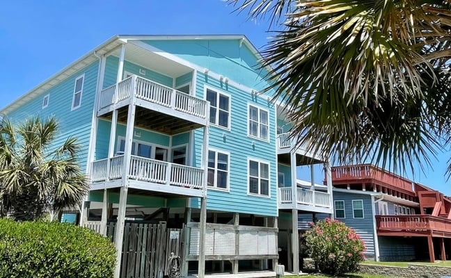 Two-story white house with wooden deck and double garage, palm trees, clear blue sky